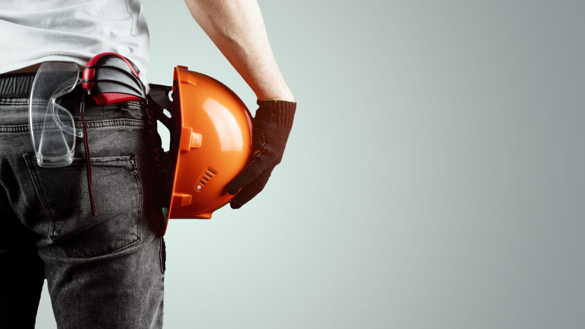 The Builder, The Architect Holds In His Hand A Construction Helmet On A Light Background, A Tape Measure.