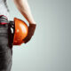 The Builder, The Architect Holds In His Hand A Construction Helmet On A Light Background, A Tape Measure.