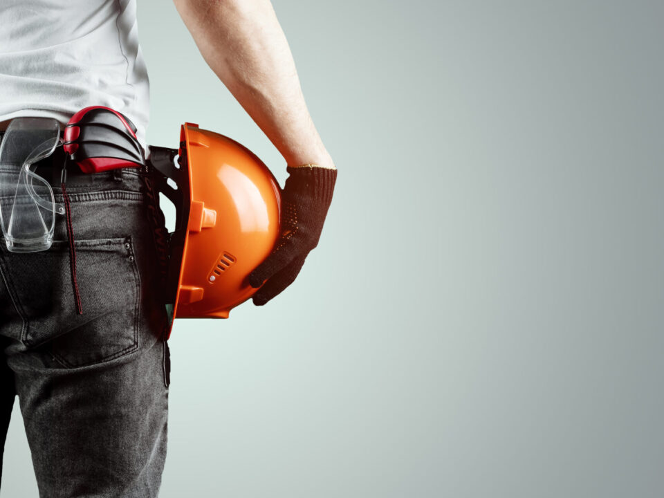 The Builder, The Architect Holds In His Hand A Construction Helmet On A Light Background, A Tape Measure.